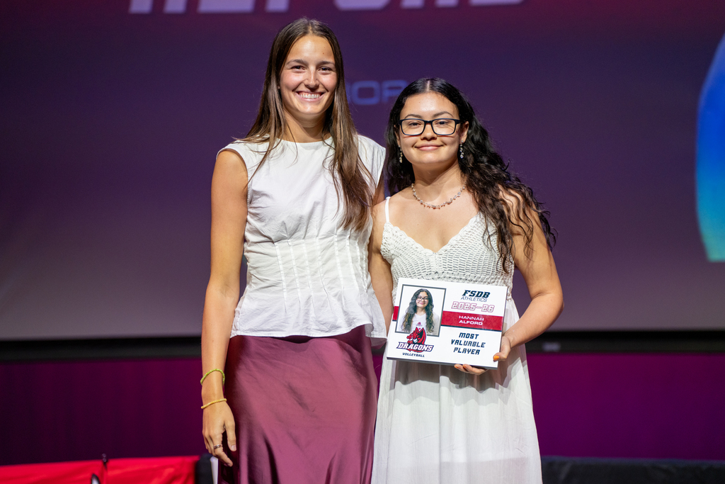 Volleyball coach smiles with a student who won an award on stage in Kirk.