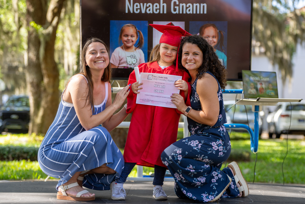Two ELC staff smile with an ELC Graduate who is holding her diploma. 