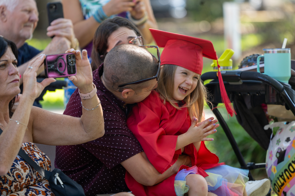 A ELC Deaf gradate smiles and claps as her Dad kisses her in the audience at Palm Row. 