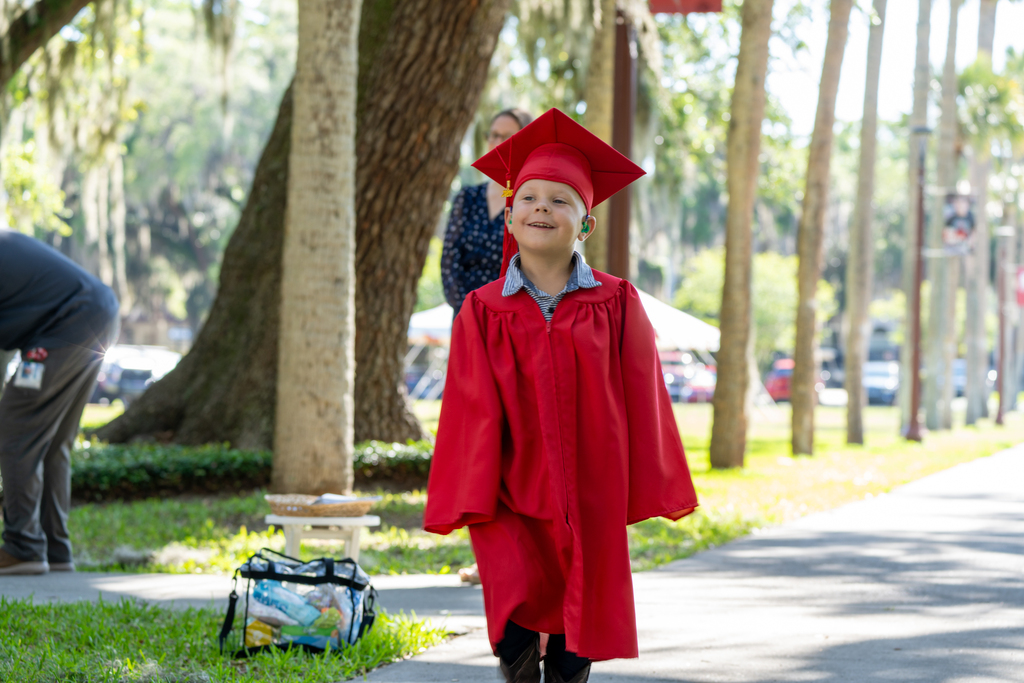 An ELC Deaf graudate wearing red cap and gown walk down Palm Row.
