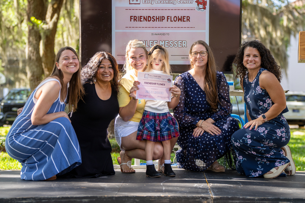 Group of ELC staff smile with a student and her mom holding her certification outside Palm Row. 