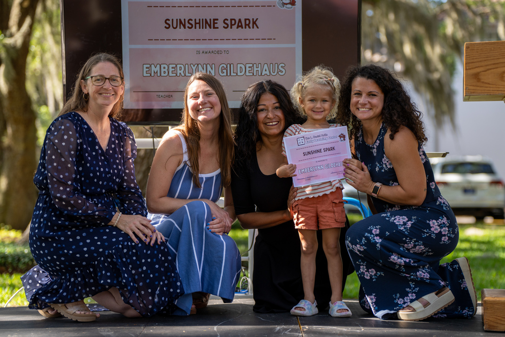 ELC staff smile with ELC student who is smiling and holding her certification outside Palm Row. 