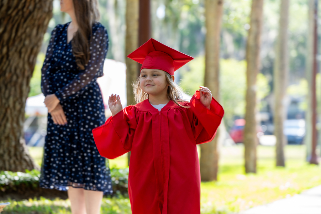 An ELC Deaf graduate wearing red cap and gown waving as she walks down Palm Row. 