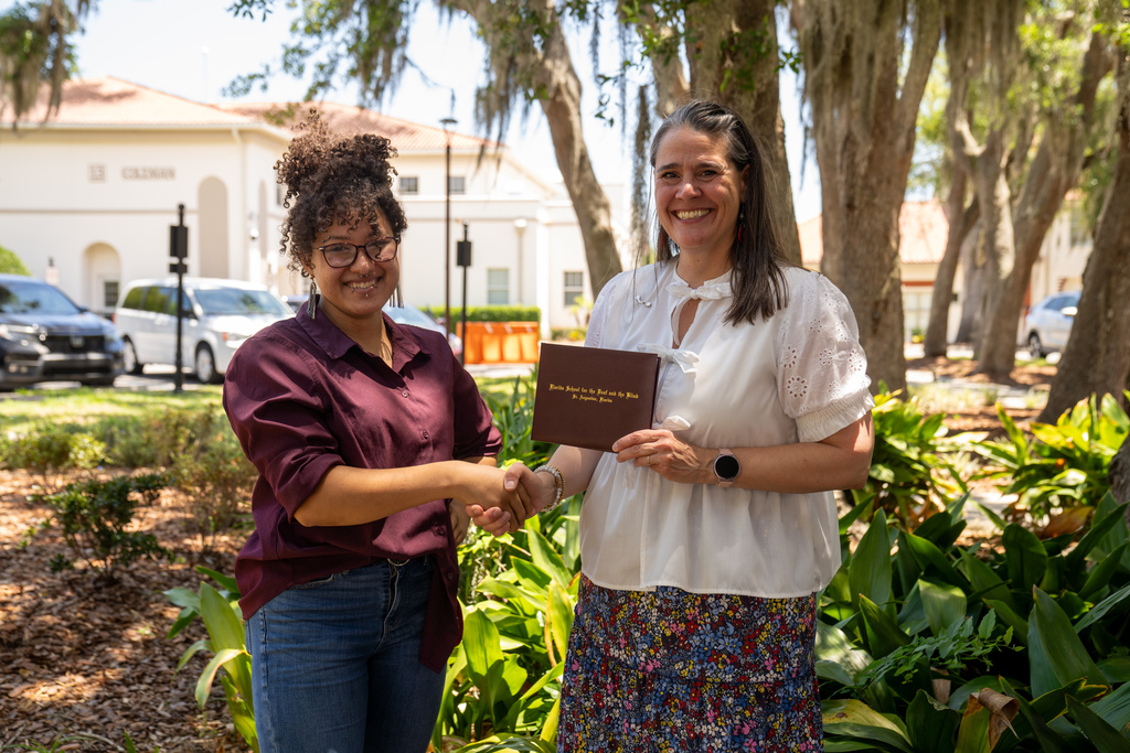 SOAR student handshake President Snow while holding his diploma outside. 