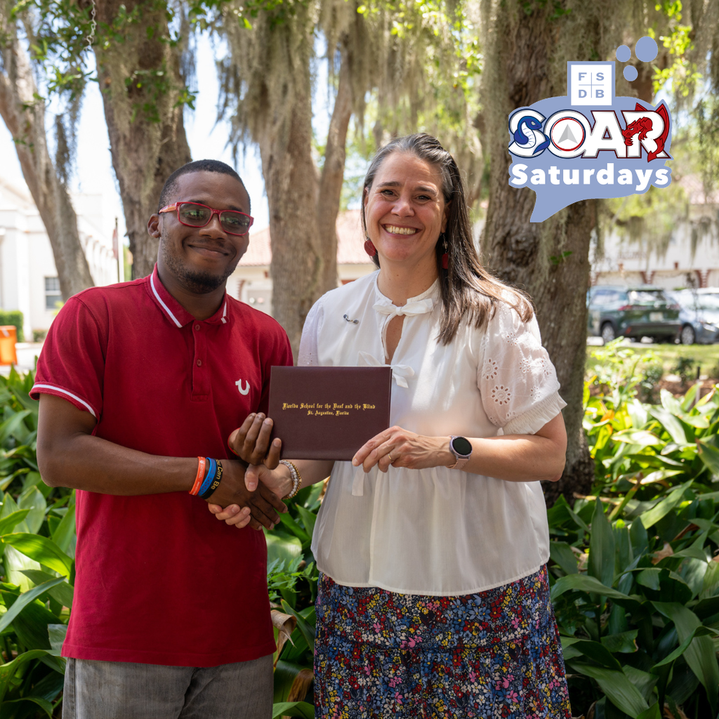 SOAR student handshake President Snow while holding his diploma outside. 