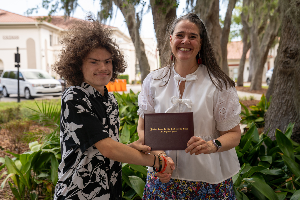 SOAR student handshake President Snow while holding his diploma outside. 
