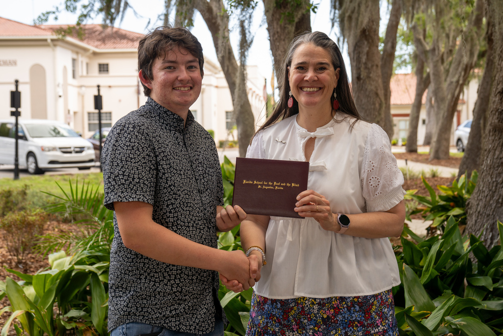 SOAR student handshake President Snow while holding his diploma outside. 