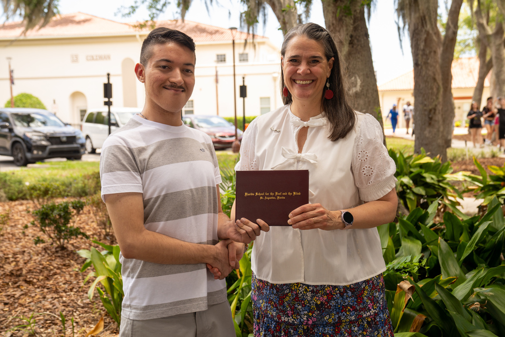 SOAR student handshake President Snow while holding his diploma outside. 