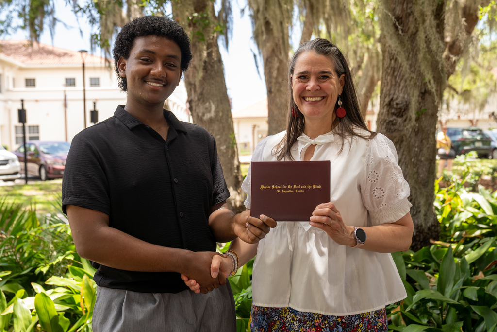 SOAR student handshake President Snow while holding his diploma outside. 