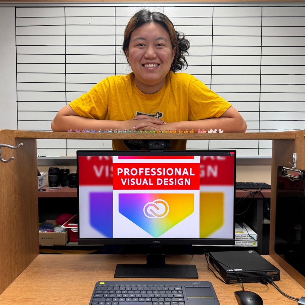 A student smiling with her computer that says "Professional Visual Design" inside a classroom.
