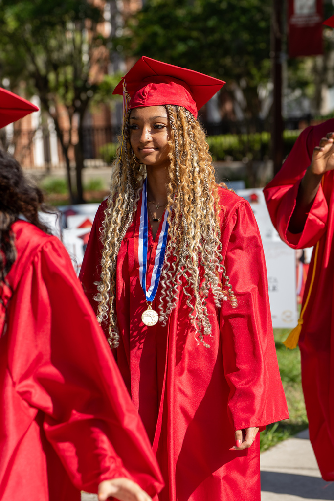 Senior dressed in red cap and gown walk outside FSDB.