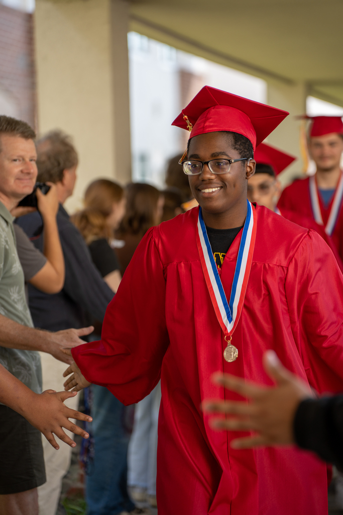 FSDB deaf senior dressed in red cap and gown high five classmate outside FSDB.