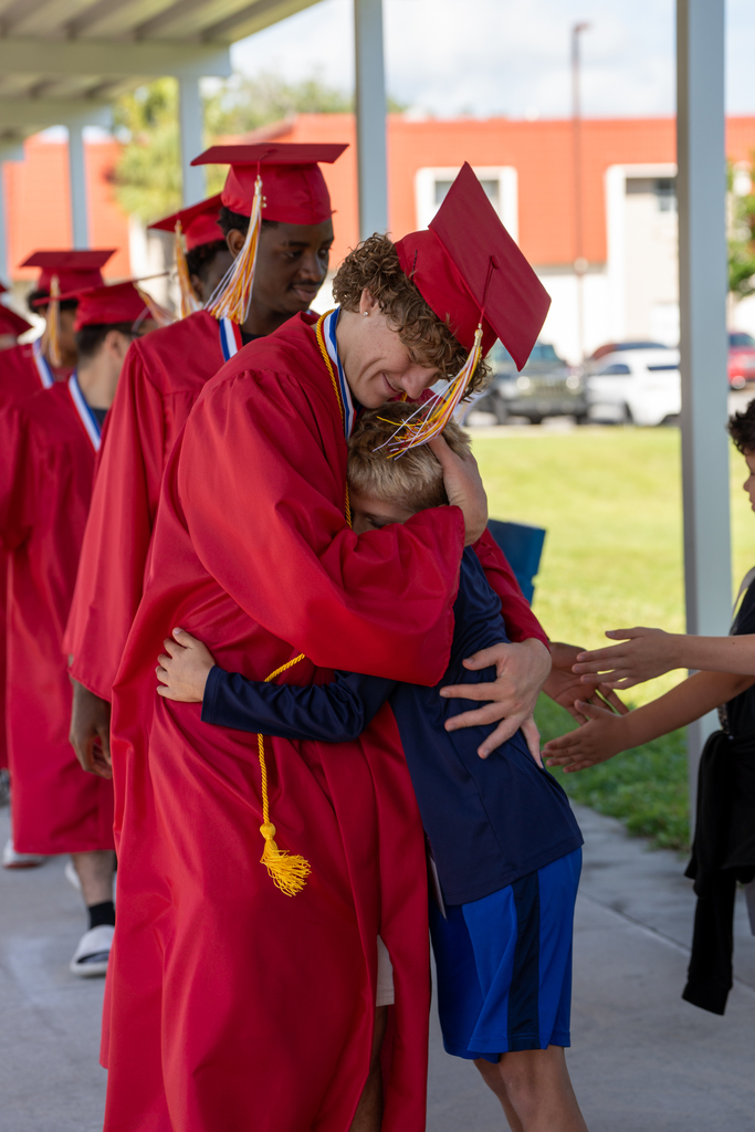 FSDB Senior dressed in red cap and gown hugs a student from elementary school.