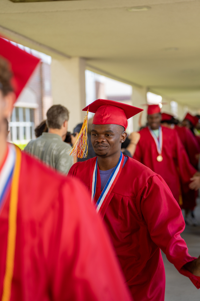 A senior dressed in red cap and gown high five classmates outside FSDB.