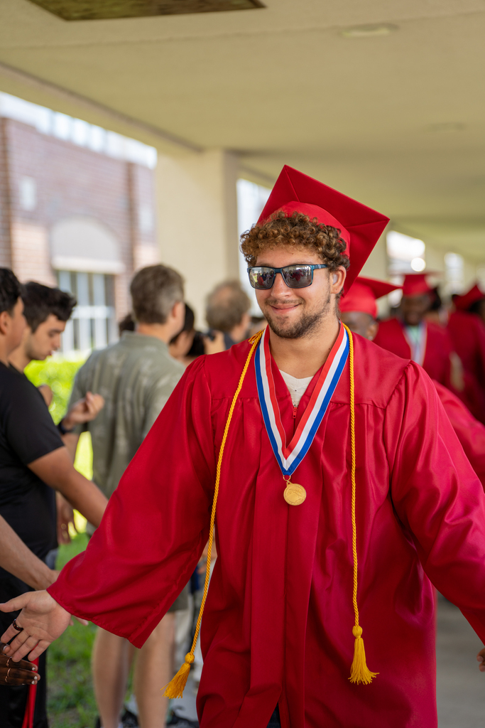 A deaf senior dressed in red cap and gown high-five his classmates outside FSDB.