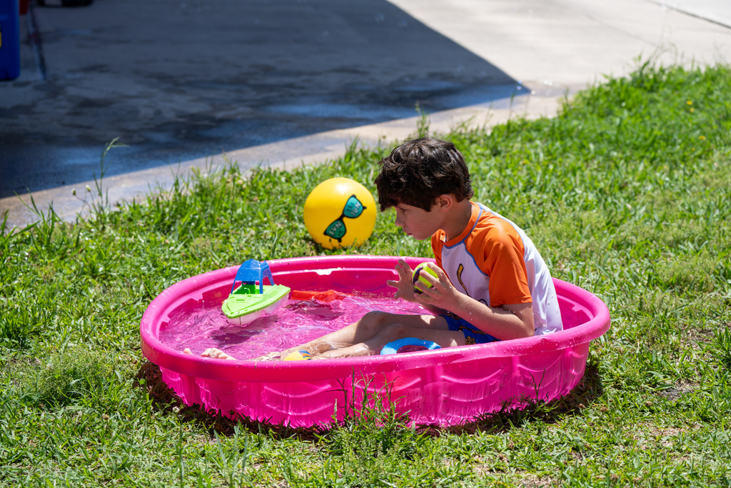 A student sits inside a pink pool playing with toys.