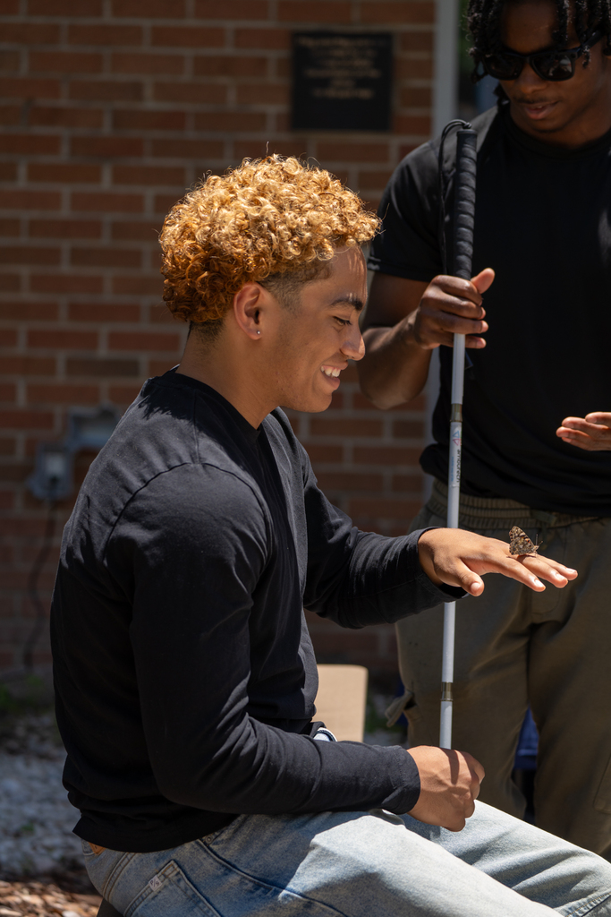 A student holding his hand out for the butterfly.
