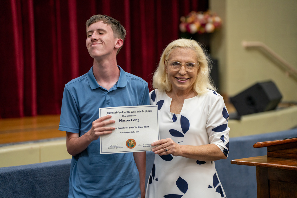 A student who won an award is smiling with the Principal of Blind Department inside the Music Building. 