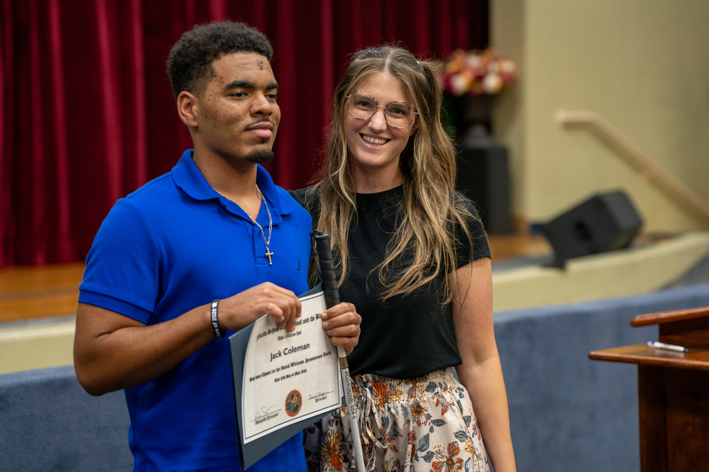 A student who won an award is smiling with a staff member inside the Music Building. 