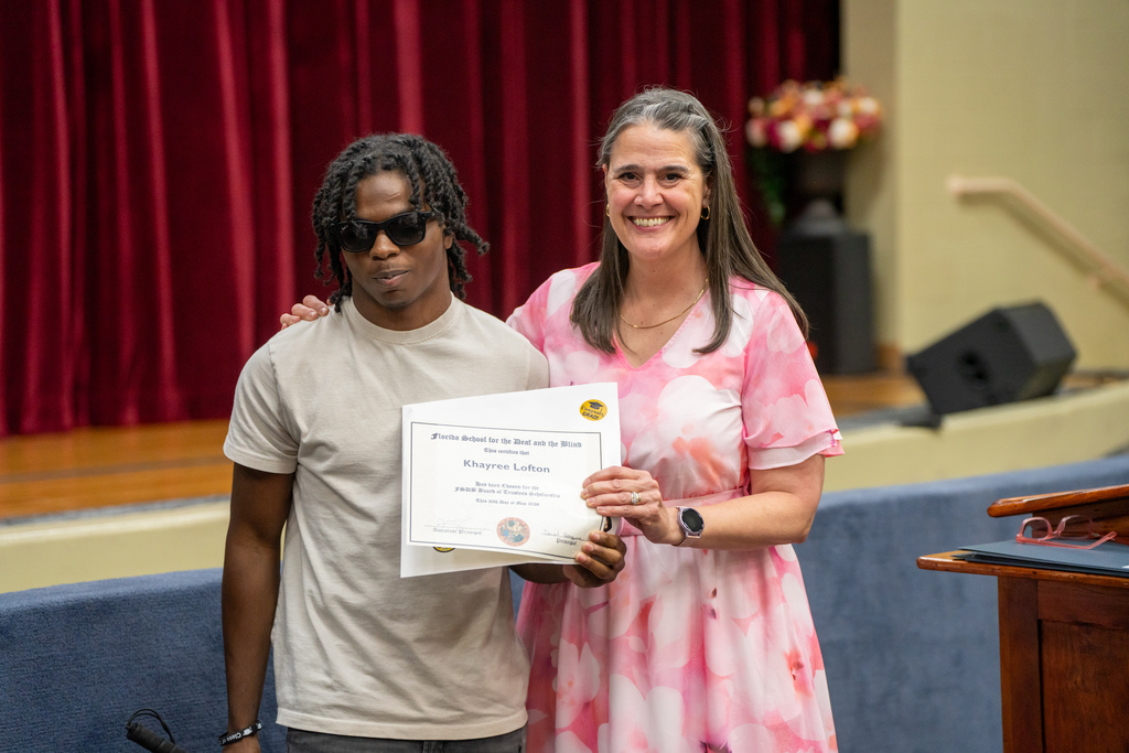 Tracie Snow is standing and smiling holding an award with a student inside the Music Building. 