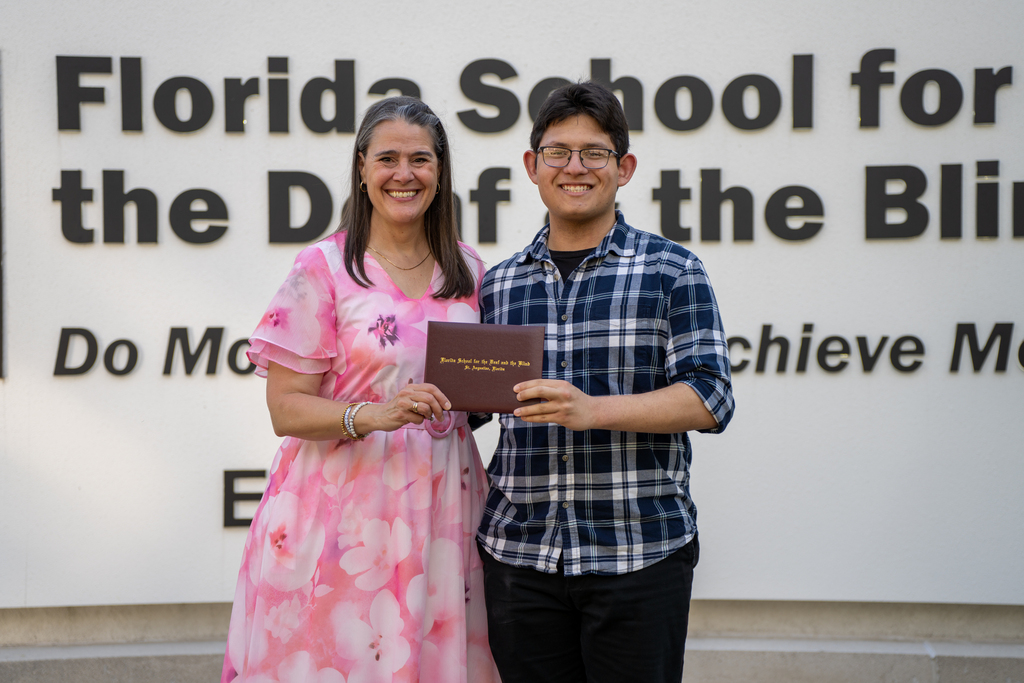 Tracie Snow smiles with a student who holds his diploma by the FSDB sign. 