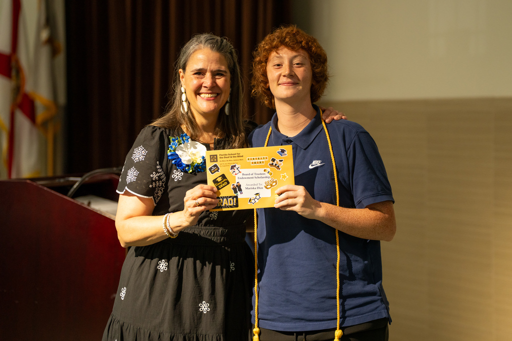 A senior smiles with Tracie Snow on stage holding an envelope.