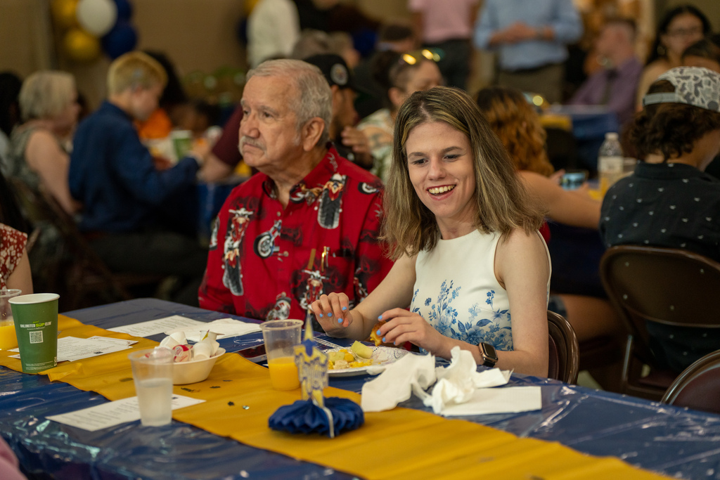 A student and her grandpa sit together at a table. 