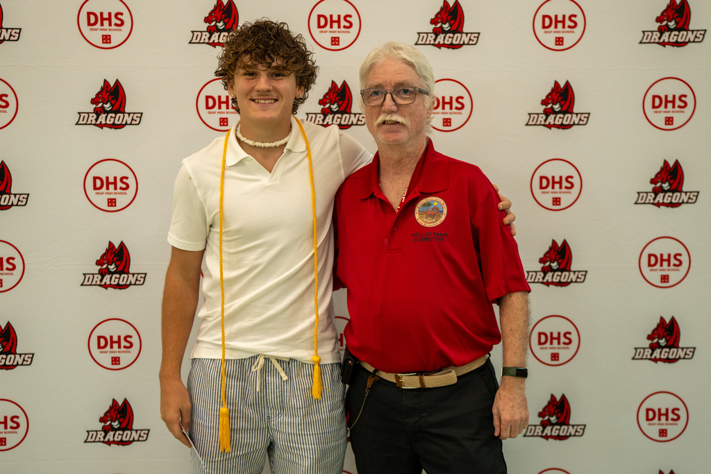 A senior smiles with BP, museum director, for a photo in front of a DHS background.