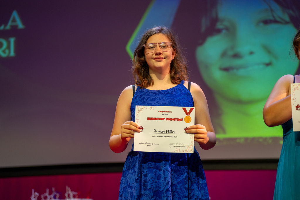 A student smiles with her award on stage in Kirk. 