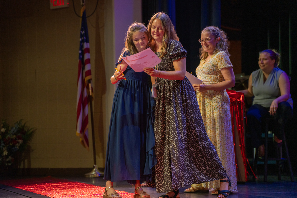 A student and a teacher hug on stage in Kirk. 