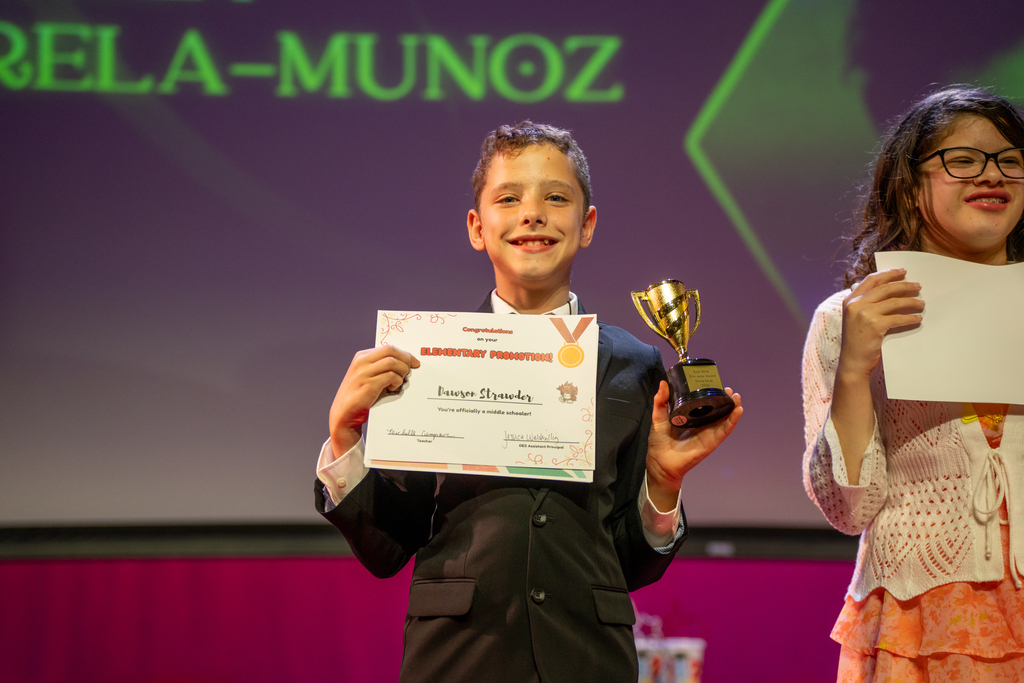 A student smiles with his awards on stage in Kirk. 
