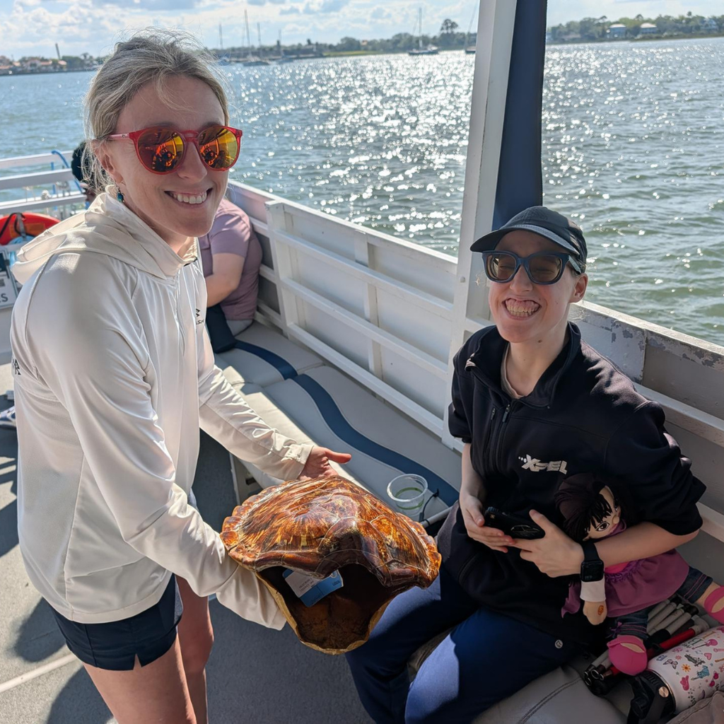 A student smiles with a female part of the Florida Water Warriors group holding a turtle shell.