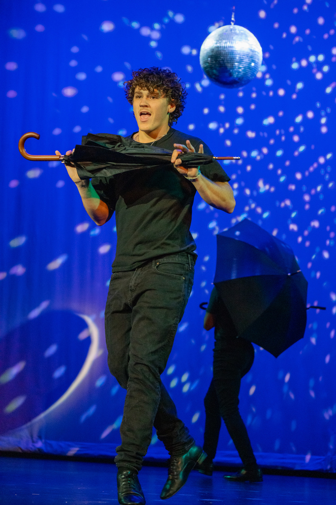 A student is dancing with an umbrella on stage in Kirk. 