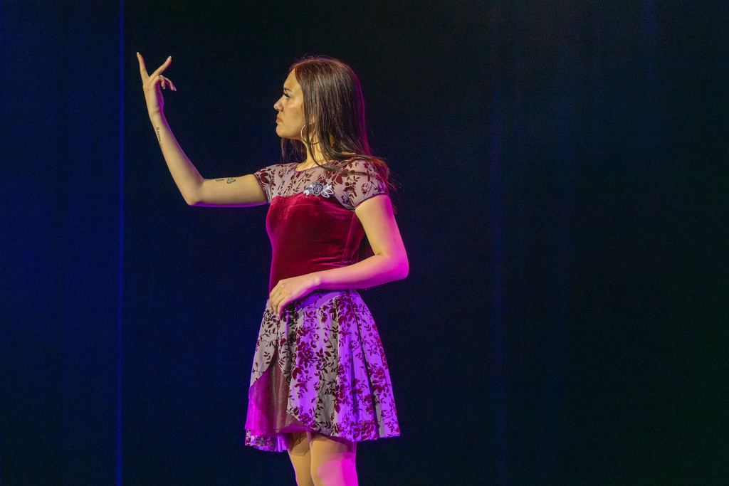 A student is wearing a maroon color dress signing on stage in Kirk. 