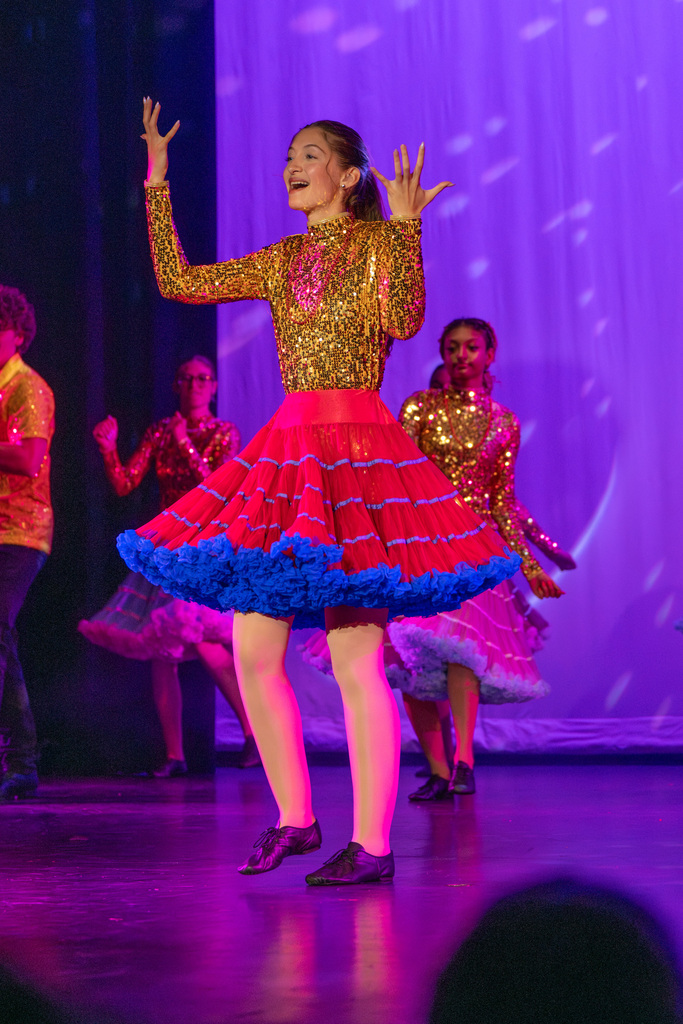 A student wearing a sparkle yellow dress and pink skirt signing on stage in Kirk. 