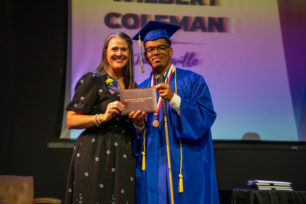 Tracie Snow smiles with a blind graduate holding the diploma on stage in Kirk. 