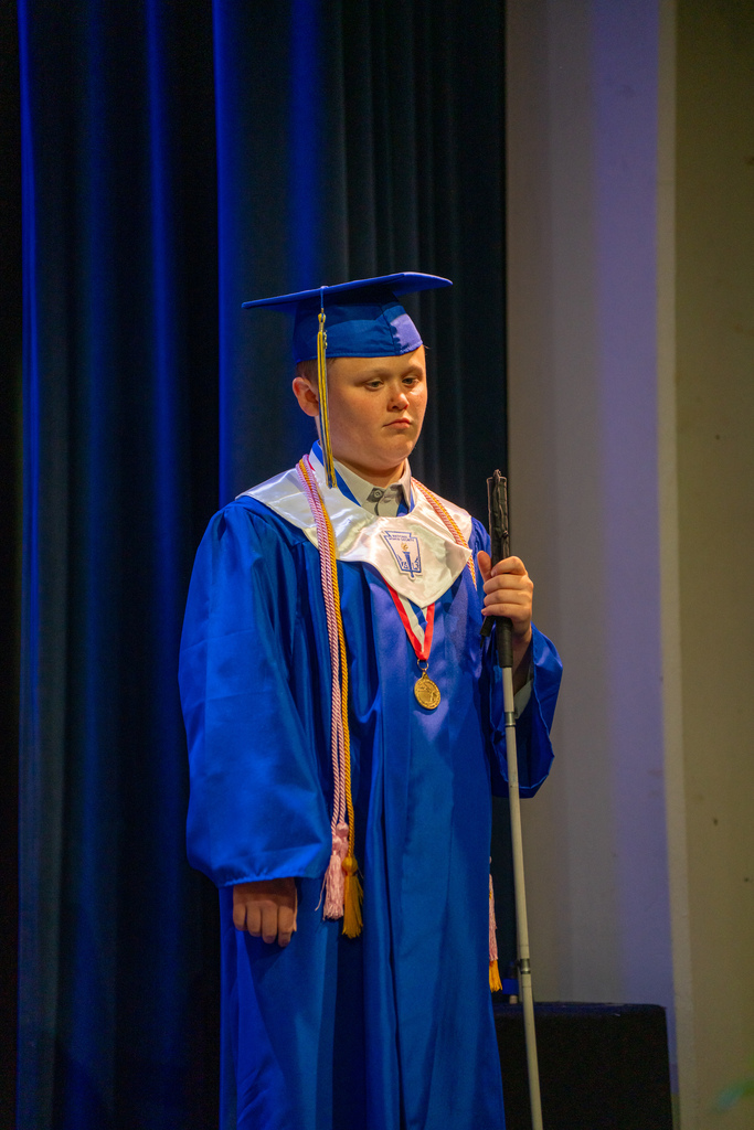 A student stands on stage in Kirk in his blue cap and gown. 