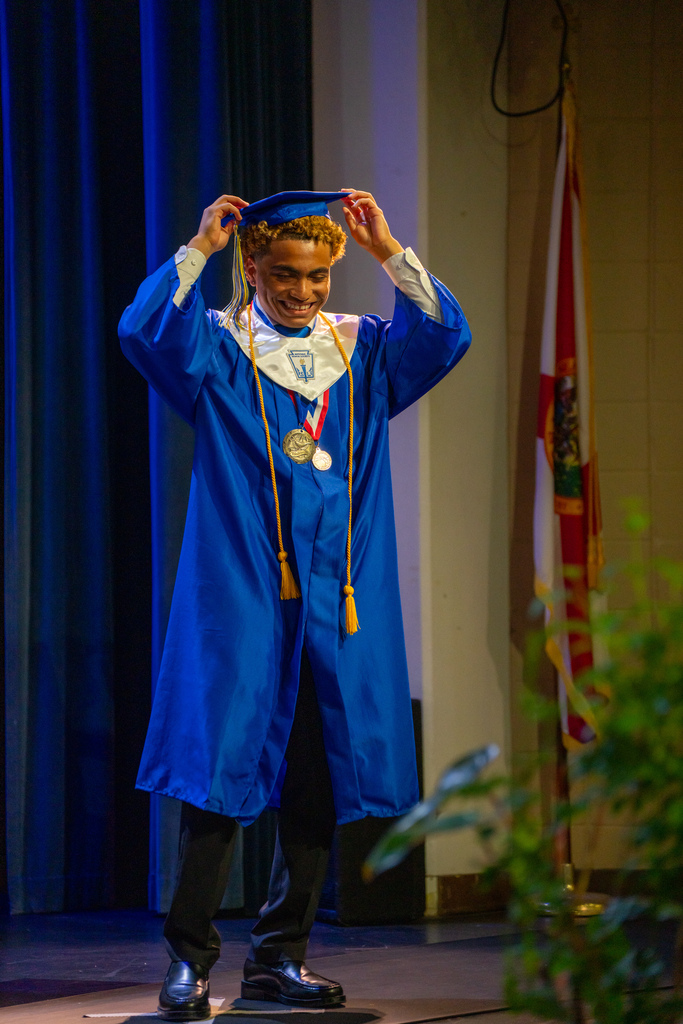 A blind student smiles on stage in his blue cap and gown. 