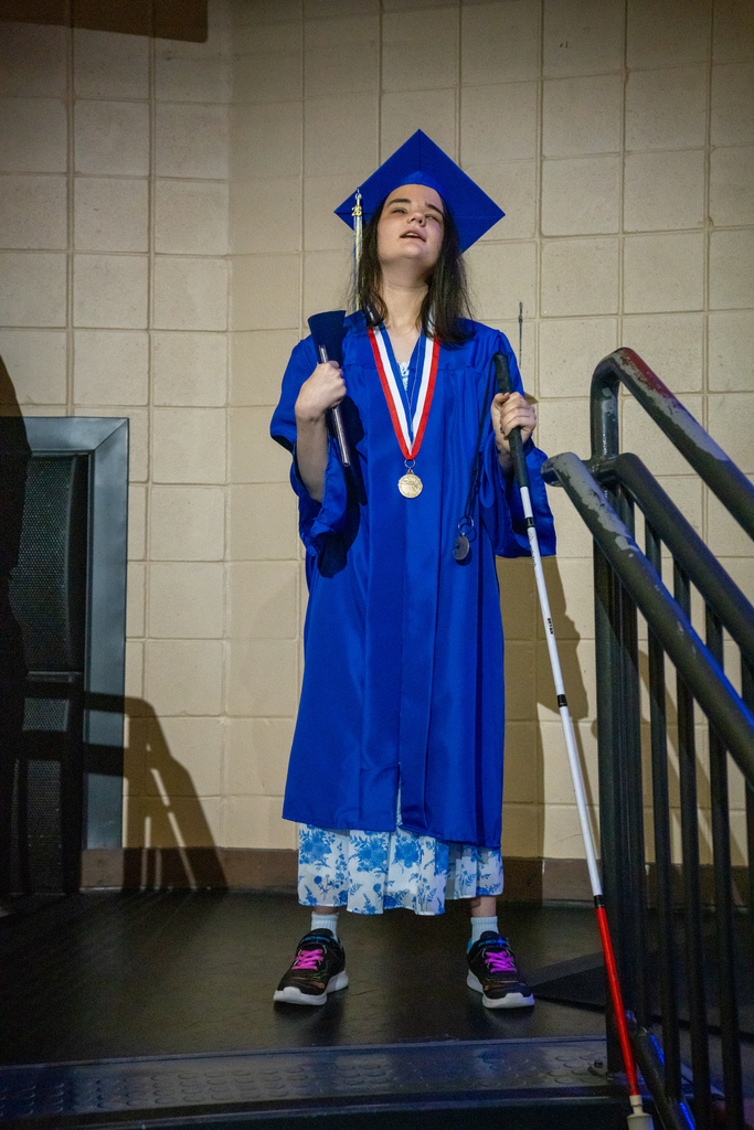 A blind graduate smile for her photo in her blue cap and gown on the stairs in Kirk. 