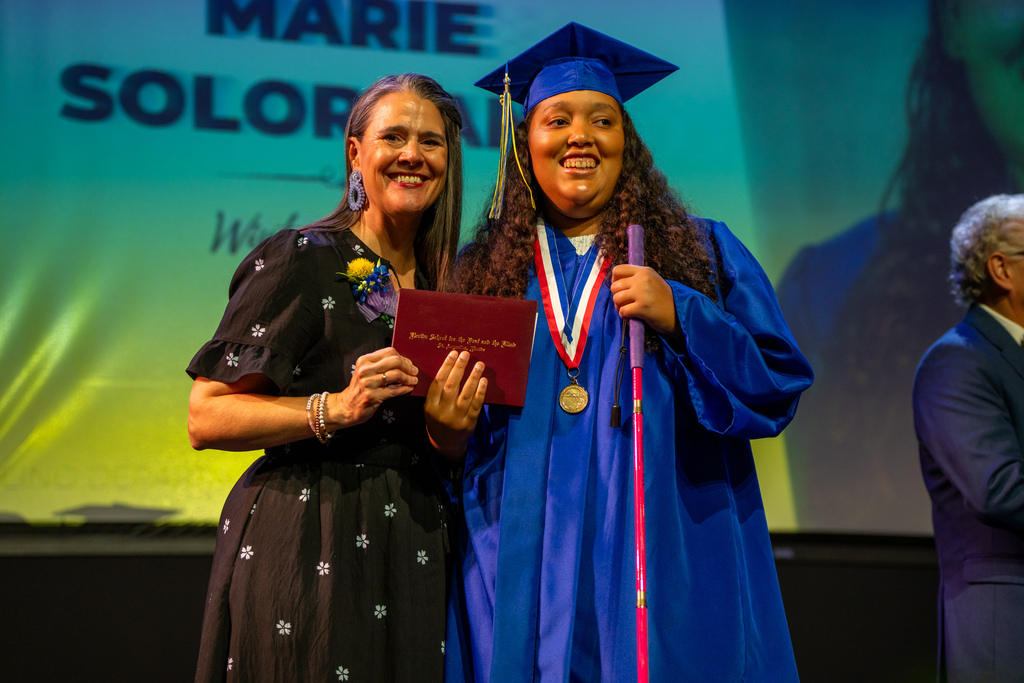 Tracie Snow holds the diploma with a blind graduate on stage in Kirk. 