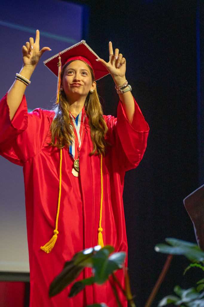 Valedictorian presents on stage in her red cap and gown. 