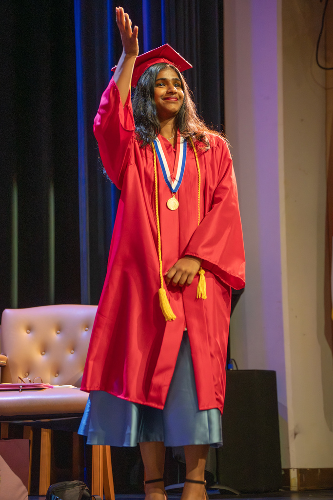 A deaf senior signs on stage in her red cap and gown. 