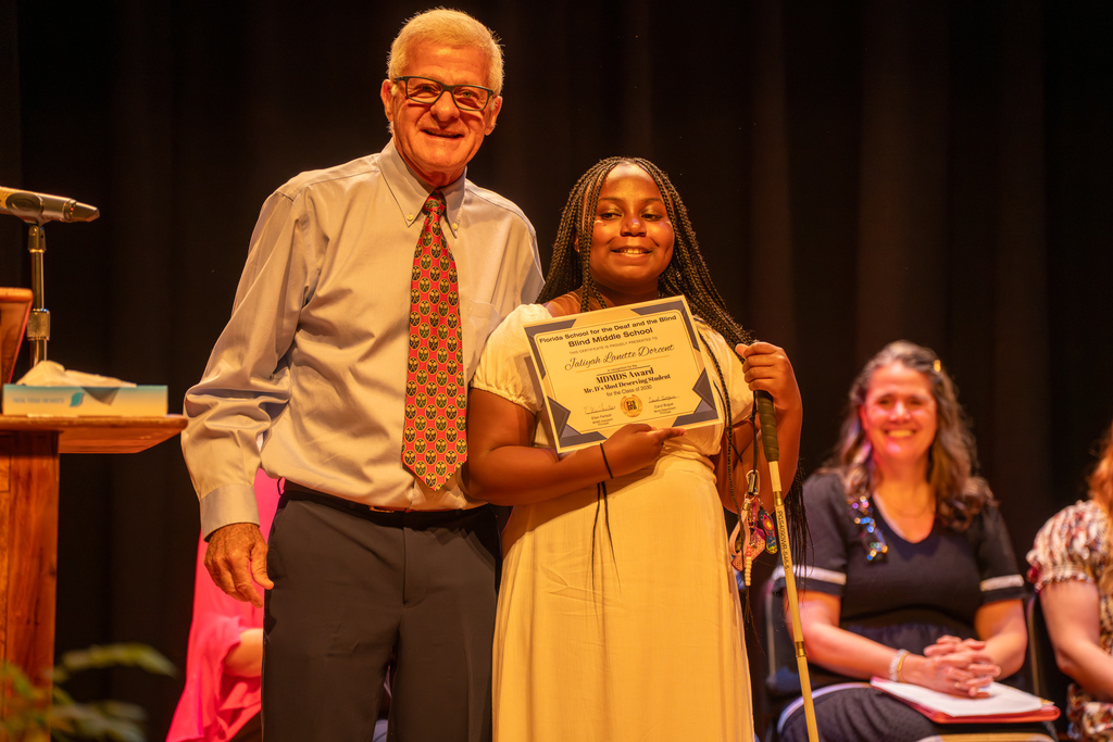 A retired staff smiles with a student who won his award smiles on stage in Music Building. 