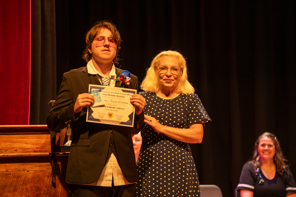 A student smiles with the blind principal with his certificate on stage in Music Building. 
