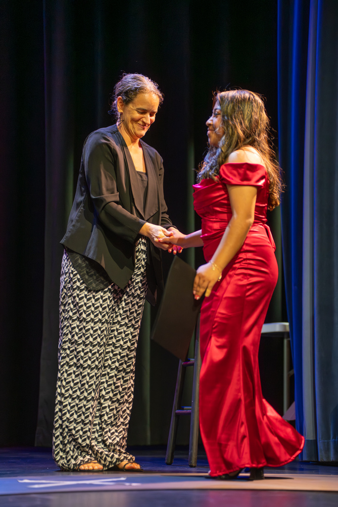 Assistant Principal of Middle School handshakes a 8th grader wearing a red dress on stage in Kirk. 