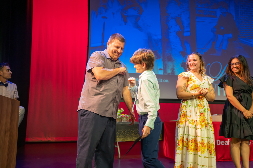 A teacher gives a student a fist bump on stage in Kirk. 