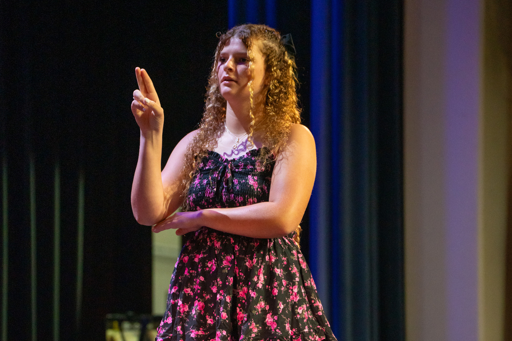 A student signs the pledge of allegiance on stage in Kirk. 