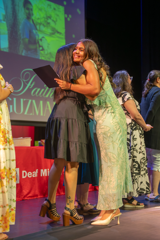 A 8th grade student hugs the 8th grade teacher on stage in Kirk. 