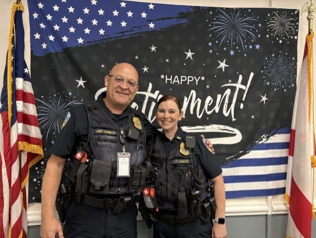 Jerry and his coworker smile for a photo with the Happy Retirement flag in background. 