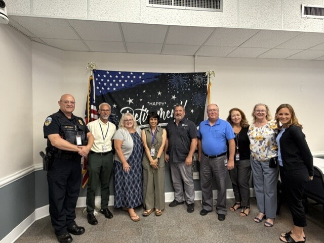 A group of co workers smile with Jerry with the Happy Retirement flag background.